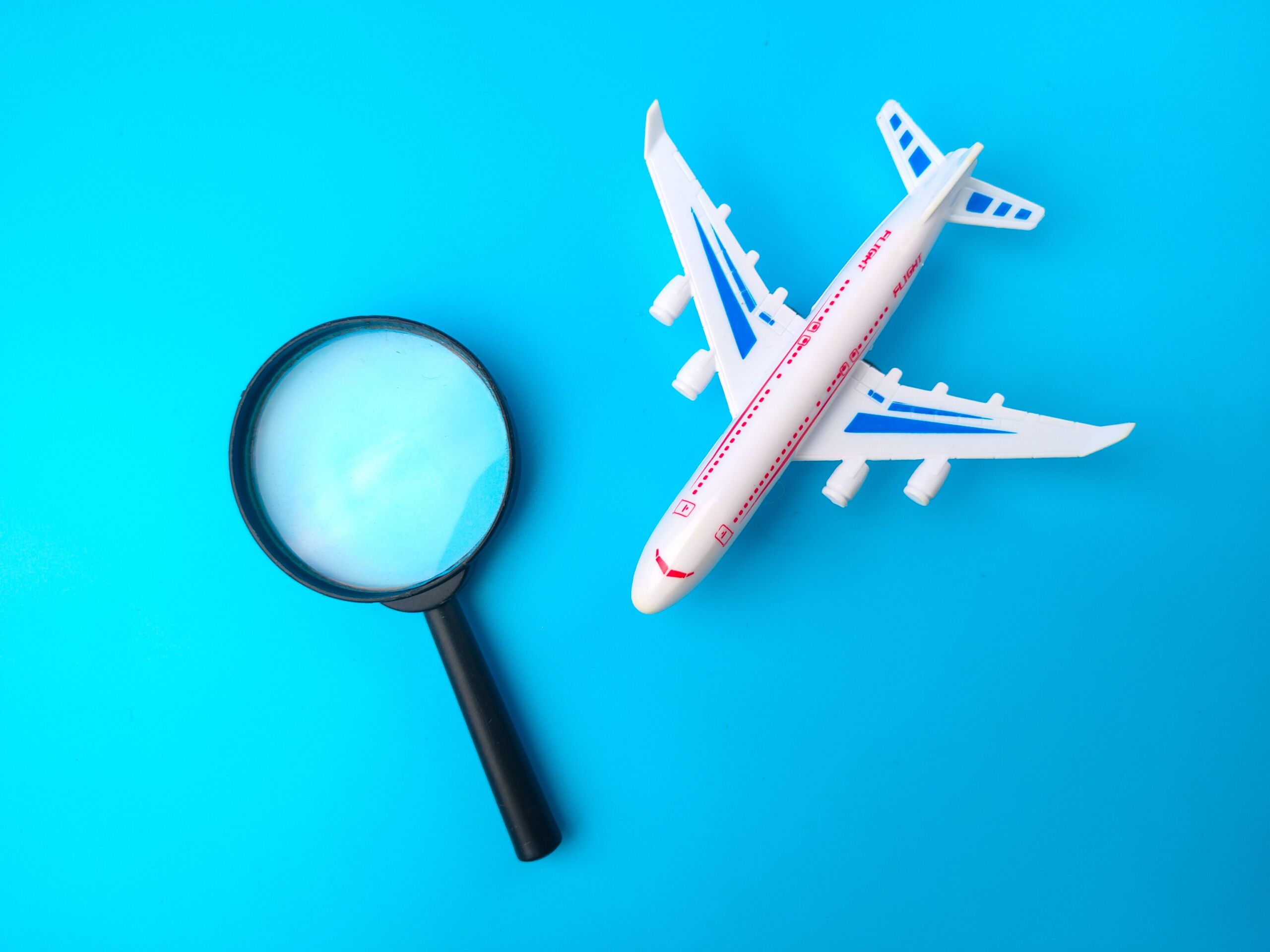 A top view of a white toy airplane and a magnifying glass isolated on an empty blue background
